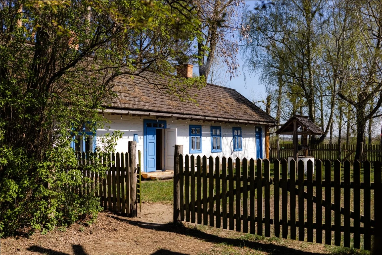 Chata w Nieborowie widziana przez otwartą drewnianą bramę